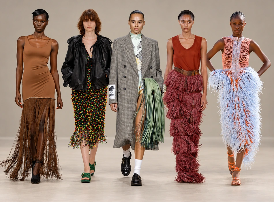 Londra Moda Haftası'nda bir defile sırasında podyumda yürüyen bir model, üzerinde hareketli ve göz alıcı uzun püsküllerle süslenmiş şık bir kıyafet sergiliyor. Bu detay, trendlerin canlılığını ve enerjisini yansıtıyor.