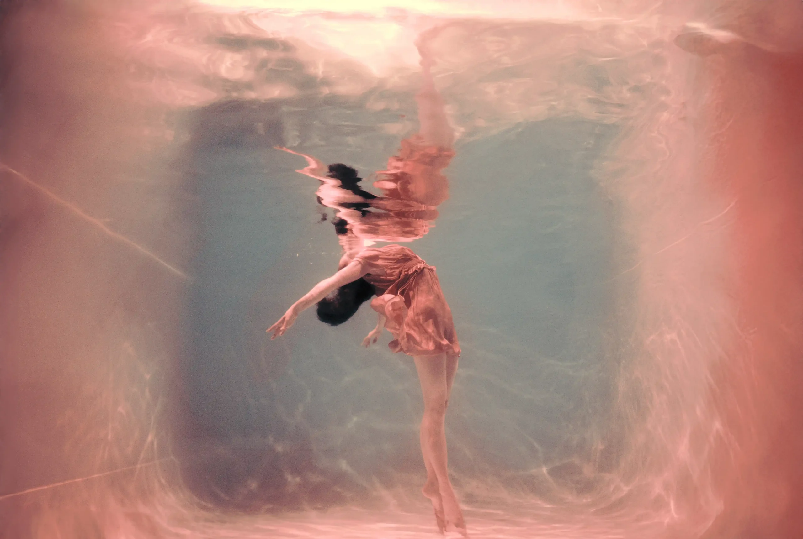 Marta Syrko'nun Immersion: Seeing Otherwise sergisinden, suyun dönüştürücü etkisiyle bedenin hatlarını değiştirdiği, saçları ıslak ve yüzü suyun altında hafifçe bulanıklaşmış, karanlık arka planda heykelsi bir figürün kırılganlığını gözler önüne seren etkileyici bir fotoğraf.