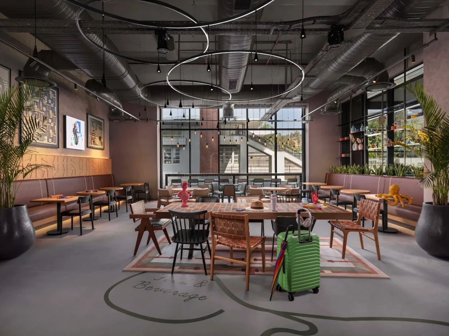 Moxy İzmir otelinin geniş, modern lobisi, deri banketler ve eklektik sandalyelerle çevrili büyük orta masa gibi farklı oturma alanları, dışarıyı gösteren yüksek pencereler ve tavandaki borular ile dairesel neon lambalarla aydınlatılmış şık endüstriyel tasarımıyla canlı bir atmosfer sunuyor.