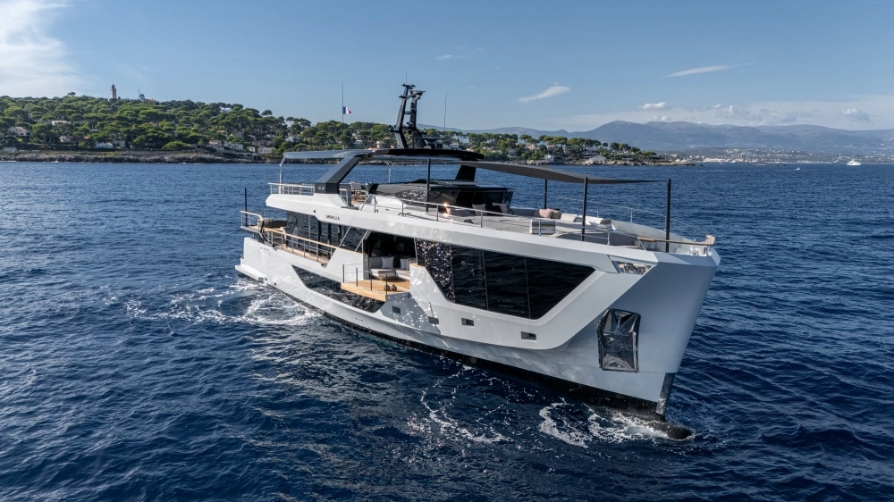 Derin mavi sularda ilerleyen modern tasarımlı beyaz ve koyu gri bir Numarine 30 XP explorer yat, lüks güverteleri ve geniş pencereleriyle dikkat çekerken, uzak planda yeşil ağaçlıklı kıyı şeridi ve bir deniz feneri görünmekte.