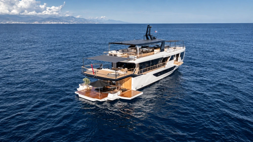 Derin mavi sular üzerinde süzülen, zarif beyaz gövdeli ve çok katlı modern bir Numarine 30XP explorer yatı, arka güvertesindeki geniş oturma alanları, ahşap zeminleri ve açılmış şemsiyesiyle dikkat çekiyor, uzakta ise dağlık bir kıyı şeridi görünüyor.