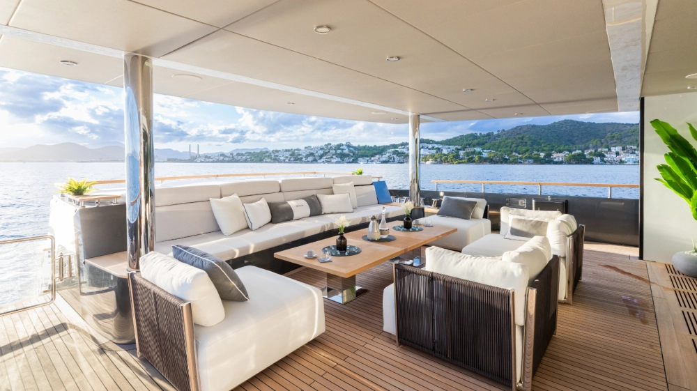 Numarine 37XP yatının arka havuzluğunda, krem rengi konforlu oturma grupları ve ahşap sehpa ile dekore edilmiş, denize nazır modern ve geniş bir açık hava yaşam alanı; huzurlu koy manzarası eşliğinde dinlenmek için ideal bir ortam sunuyor.
