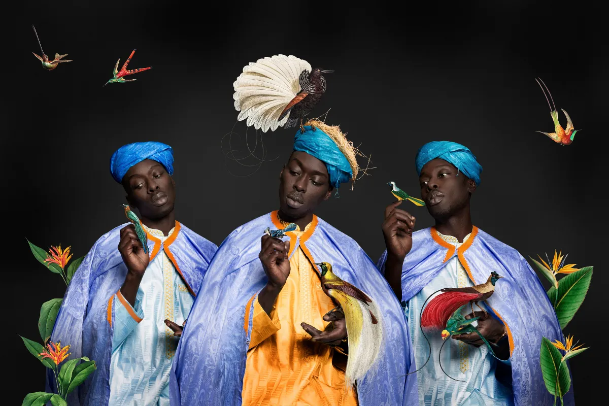 212 Photography Istanbul programında yer alan Omar Victor Diop'un, canlı renklerle tasarlanmış geleneksel desenli kıyafetleri ve başlığıyla, dikkat çekici mavi bir fon önünde sakin ifadesiyle izleyiciye bakan bir adamın estetik ve kurgulu portresi.