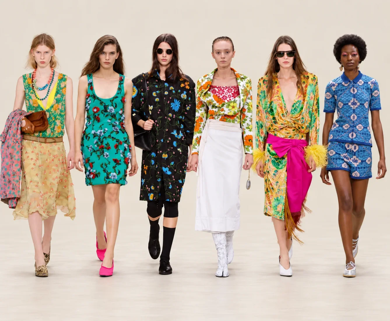 Paris Moda Haftası'nda podyumda yürüyen, geniş kenarlı şapkası, büyük güneş gözlükleri, desenli dökümlü elbisesi ve çizmeleriyle 70'li yıllar modasının ikonik tarzını sergileyen bir manken.