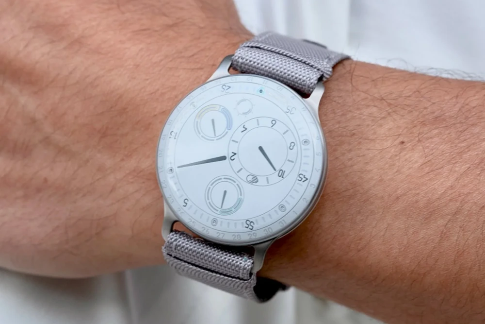 Ressence Type 3 kol saatinin, saatin ibrelerinin ve alt kadranlarının sıvı benzeri bir ekran altında yüzüyormuş gibi göründüğü, kendine özgü disklere dayalı göstergesini vurgulayan yakın çekim görüntüsü.