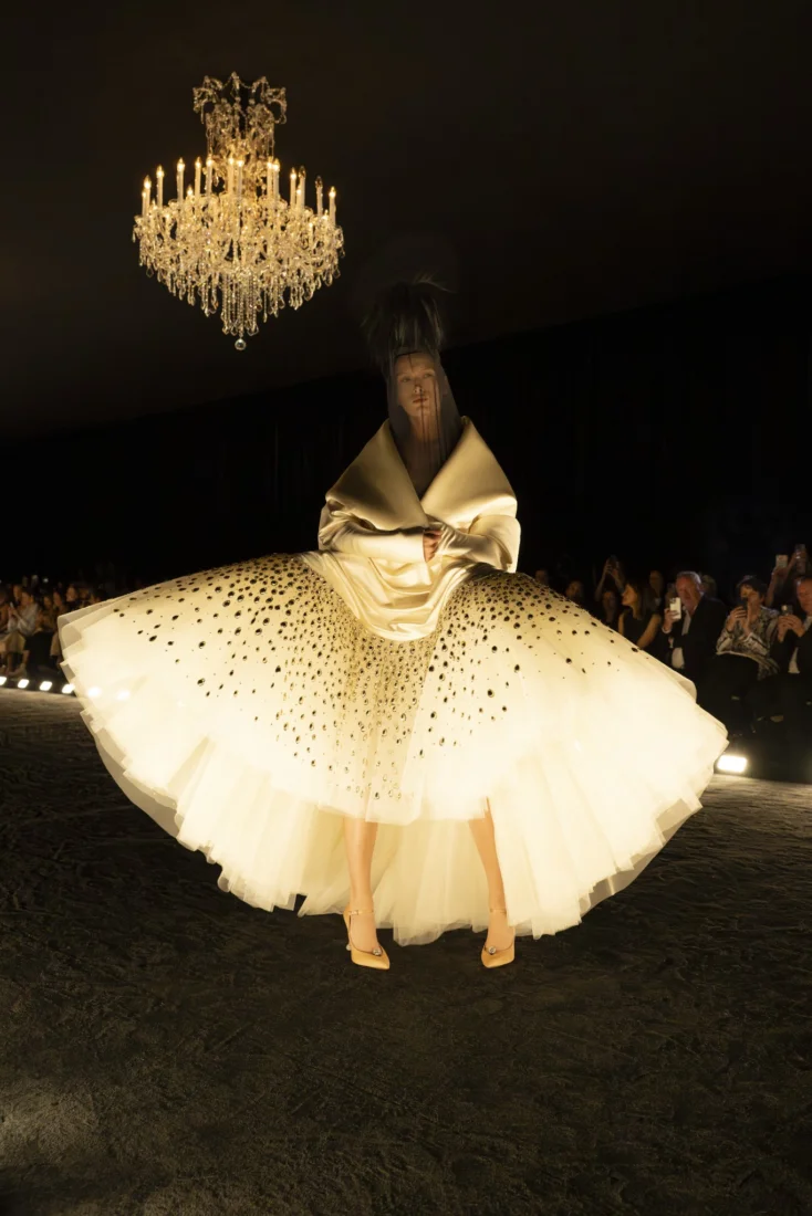 Bir model, Schiaparelli'nin sürrealist mirasını ve avangart estetiğini yansıtan, yenilikçi tasarımı, lüks dokuları ve büyüleyici detaylarıyla öne çıkan çarpıcı bir haute couture kıyafetini sergiliyor.