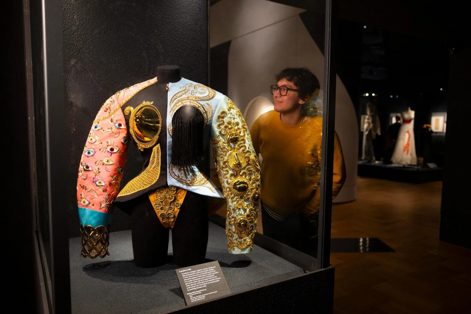 Victoria and Albert Museum'daki Schiaparelli: Fashion Becomes Art sergisinden bir görünümde, modern bir galeride özenle aydınlatılmış mankenler üzerinde sergilenen, Elsa Schiaparelli'nin sanatsal ve sürrealist yaklaşımlarını yansıtan detaylı ve ikonik haute couture kıyafet tasarımları dikkat çekiyor.