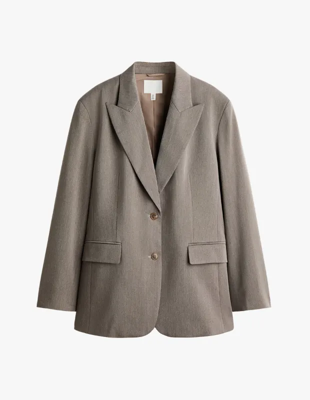 Açık bej-gri tonlarında, hafif dokulu keten görünümlü kumaşıyla öne çıkan, geniş yakalı, iki düğmeli ve önünde kapaklı cepleri bulunan bu oversize blazer ceket, seyahat stil rehberinizde konforlu ve şık bir görünüm yakalamak için çok yönlü bir parça.