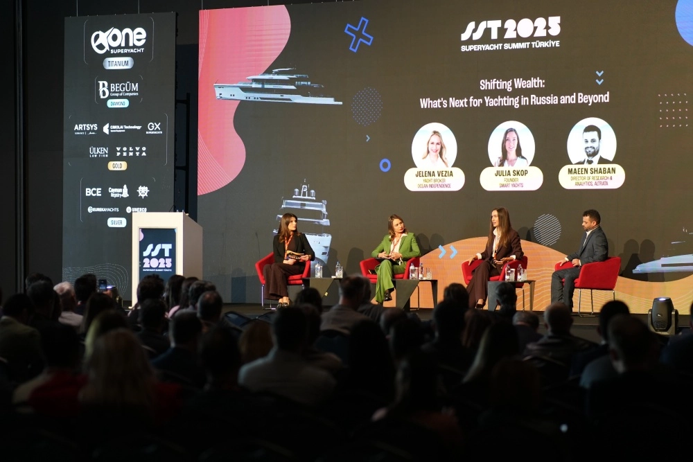 Süper Yat Zirvesi Türkiye konferansının önemli bir panel oturumunda, etkinlik logosunun belirgin bir şekilde sergilendiği ışıklı sahne panelinin önündeki uzun masada yan yana oturan uzman konuşmacılar, bir moderatör eşliğinde mikrofonlar aracılığıyla sektördeki güncel gelişmeleri ve gelecek vizyonunu katılımcılarla paylaşıyor.
