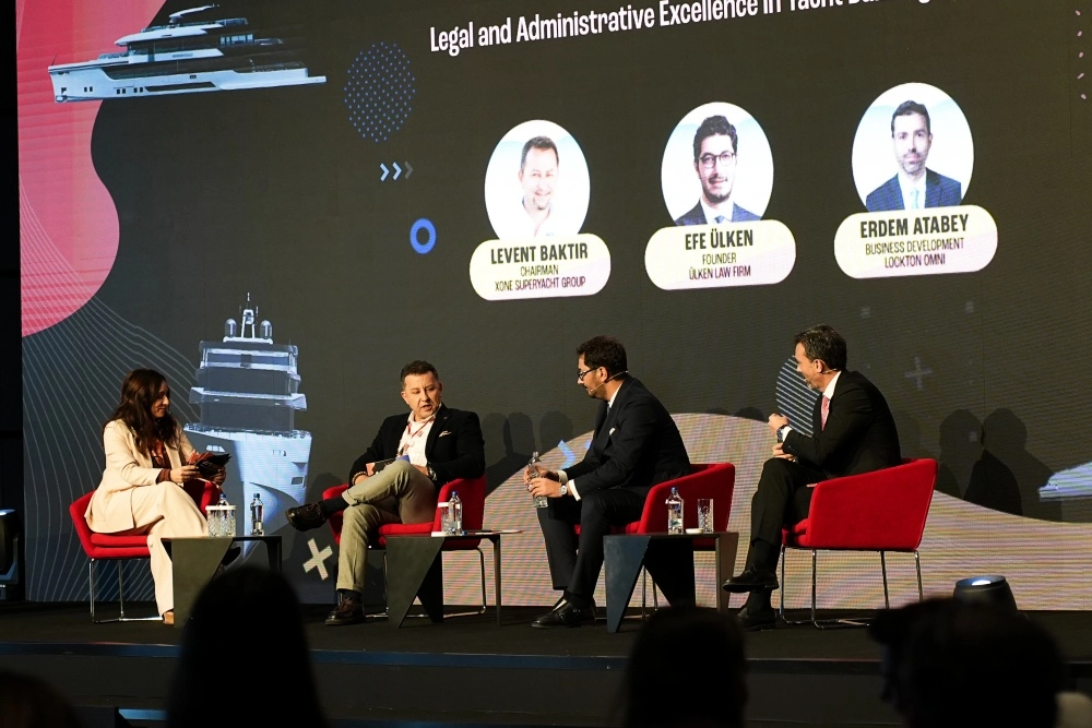 Super Yacht Summit Türkiye konferansı kapsamında düzenlenen bir panelde, sektörün önde gelen uzmanları ve temsilcileri, sahnedeki uzun masada oturmuş, dinleyicilere yönelik önemli tartışmalar yaparken, arkalarındaki geniş ekranda ilgili sunum görselleri yansıtılıyor.