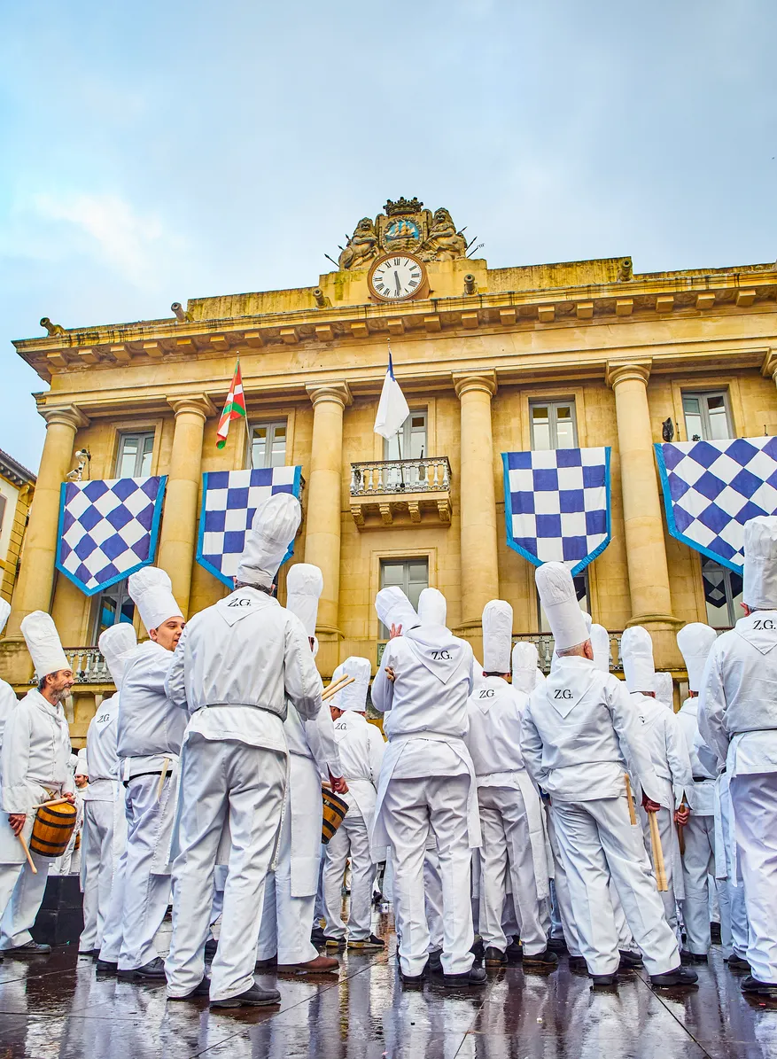 San Sebastián sokaklarında geçen Tamborrada festivalinde, geleneksel şef ve askeri üniformalarla bir araya gelmiş kalabalık davulcuların coşkulu ritimlerle şehri şenlendirdiği ve kutlama atmosferi yarattığı canlı bir an.