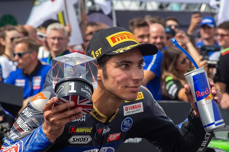 2022 yılındaki bir yarışta mavi ve beyaz Yamaha motosikletiyle keskin bir virajı dönerken dizini yere değdirecek kadar yatmış Toprak Razgatlıoğlu, tam odaklanmış bir şekilde hızla ilerliyor.