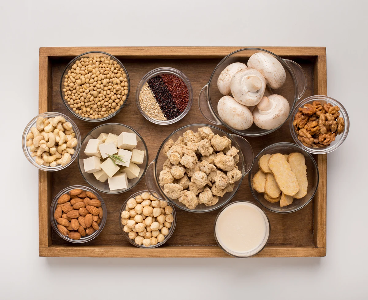 Zengin bir besin değeri sunan ve vegan beslenme için hayati önem taşıyan protein kaynaklarını sergileyen bu görselde, mercimek, nohut, badem, kabak çekirdeği ve kinoa gibi çeşitli bitkisel gıdalar estetik bir düzenlemeyle bir araya getirilmiştir.