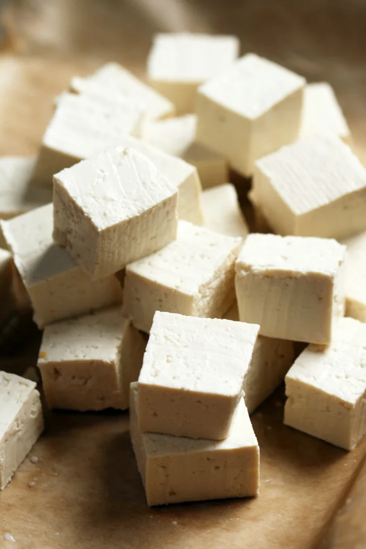 Ahşap bir masa üzerinde beyaz bir tabakta, altın rengi kızarmış ve özenle hazırlanmış küp şeklindeki tofu parçaları, taze yeşillikler ve renkli sebzelerle dengeli bir öğün oluşturarak vegan protein arayanlar için cazip bir seçenek sunuyor.