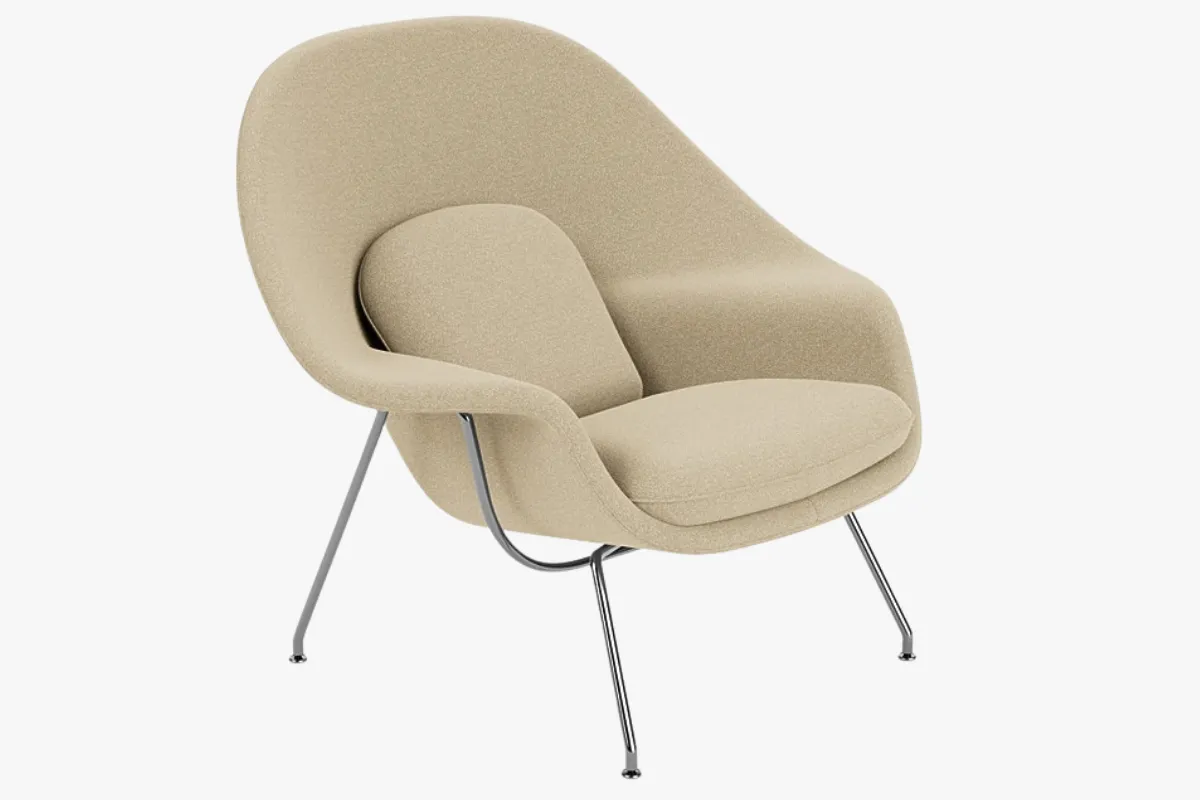 Eero Saarinen tarafından tasarlanan ve kavisli, kucaklayıcı formuyla dikkat çeken, açık renk kumaş döşemeli ve minimalist siyah metal iskeletli Womb Sandalyesi, modern mobilya tasarımının zamansız ve ikonik bir örneği olarak zarif bir iç mekanda duruyor.