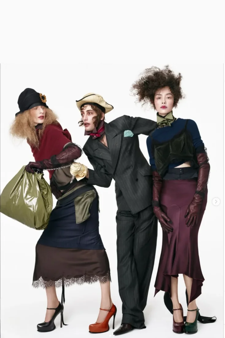 Model, kalın omuzlu ve hacimli koyu renk bir ceket ile açık renk bir içlik giyerek dinamik bir poz veriyor; bu görünüm, Zara'nın John Galliano tasarımlarından esinlenen modern ve dramatik estetiğini vurguluyor.