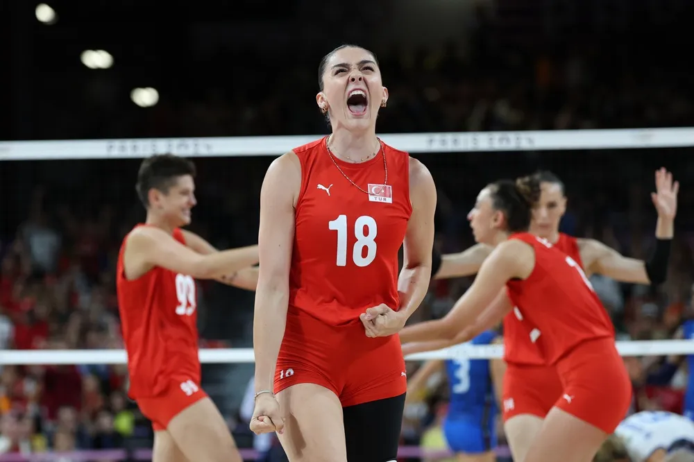 Milli voleybolcu Zehra Güneş, kırmızı Türkiye forması ve 18 numarasıyla voleybol sahasında büyük bir coşku içinde bağırarak ve yumruklarını sıkarak kazanılan bir sayıyı kutluyor; bu an, onun kariyeri boyunca sergilediği tutkulu ve mücadeleci karakterini gözler önüne seriyor.