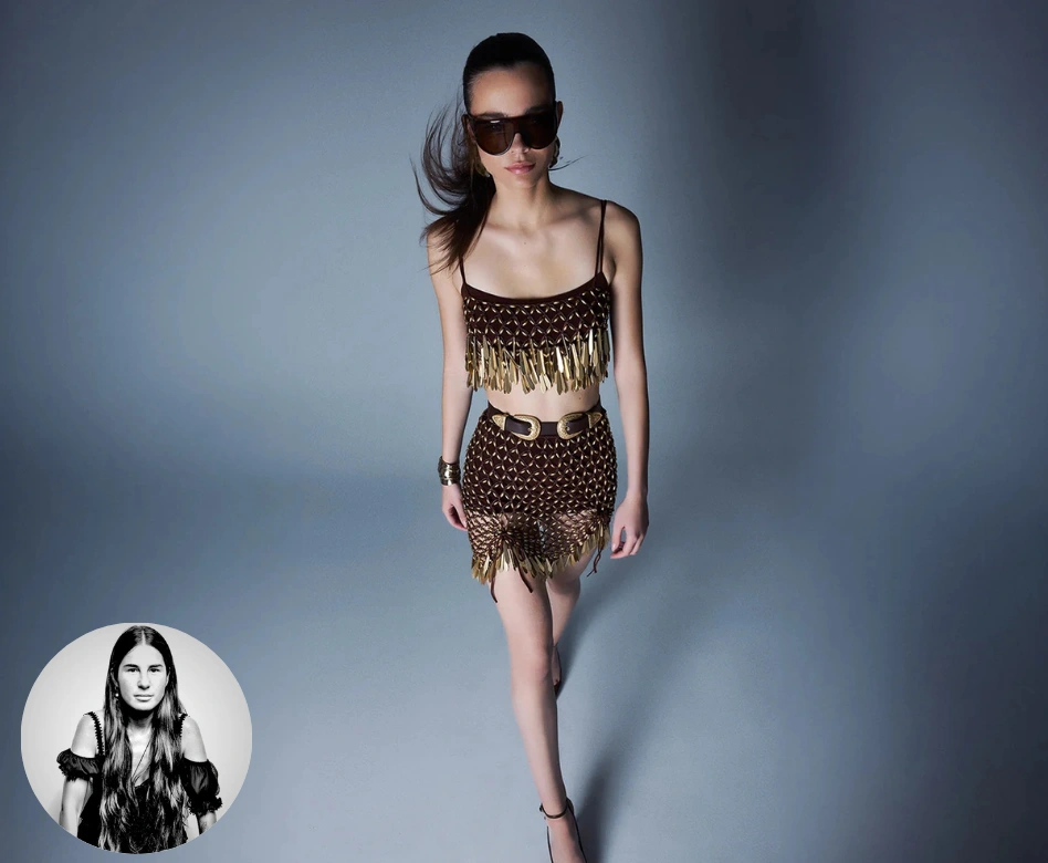 Model, Zeynep Tosun'un özgün tasarımlarından, metalik püsküllü kahverengi bir büstiyer ve uyumlu kemerli mini etek takımıyla kararlı adımlarla ilerlerken, büyük güneş gözlükleri ve rüzgarda savrulan saçlarıyla dikkat çekiyor; fotoğrafın sol alt köşesinde tasarımcı Zeynep Tosun'un siyah beyaz portresi bulunuyor.
