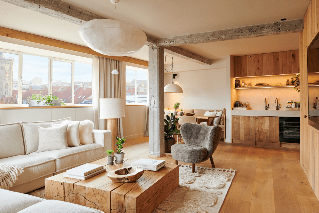 Kopenhag'daki bir otel odasının aydınlık ve ferah iç görünümü, beyaz nevresimli konforlu çift kişilik yatağı, zarif ahşap duvar panelleri, minimalist bir masa ve iki sandalyesiyle dingin bir atmosfer sunarak misafirlerini dinlenmeye davet ediyor.