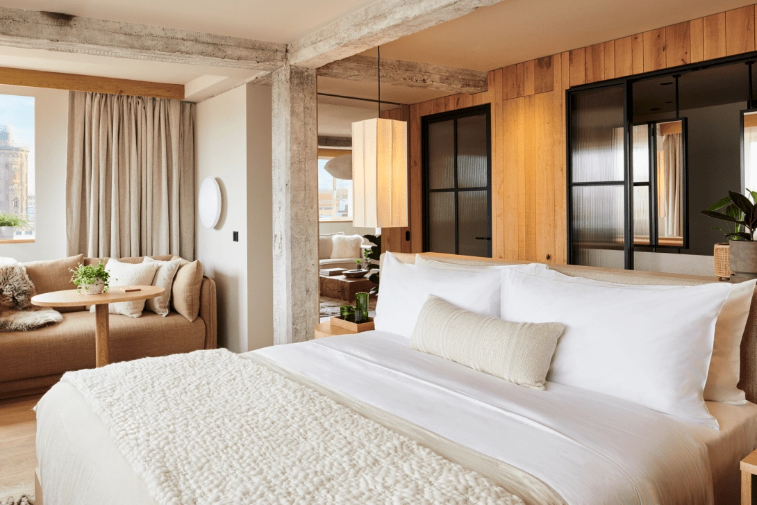 1 Hotel Copenhagen'ın aydınlık lobisi, geniş pencerelerden içeri süzülen doğal ışıkla parlayan, ahşap detaylar ve toprak tonlarındaki tekstillerle döşenmiş konforlu oturma gruplarını ve canlandırıcı bitki düzenlemelerini gözler önüne seriyor.
