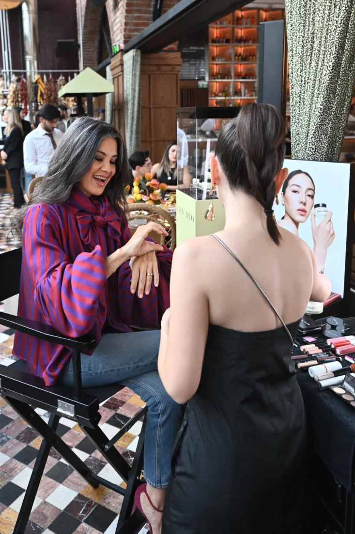 Bobbi Brown Vitamin Enriched Face Base+ kremi, OGGUSTO ve Bobbi Brown Cosmetics iş birliğiyle düzenlenen Vitamin Enriched Breakfast Club etkinliğinde, güne zinde bir başlangıcı simgeleyen taze meyveler, narenciye dilimleri ve çeşitli kahvaltılıklarla süslenmiş şık bir masada sergileniyor; arka plandaki yeşil bahçe ortamı huzurlu atmosferi pekiştiriyor.