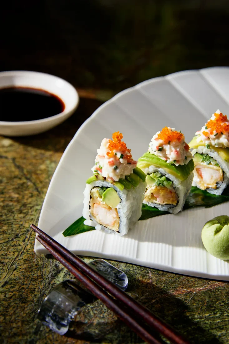 Beyaz dikdörtgen bir servis tabağında, yeşil yosun veya avokado ile sarılmış, üzerinde parlak turuncu balık havyarı, beyaz mayonez bazlı sos ve taze dereotuyla bezenmiş Kelebek Roll sushi parçaları estetik bir şekilde sergileniyor.