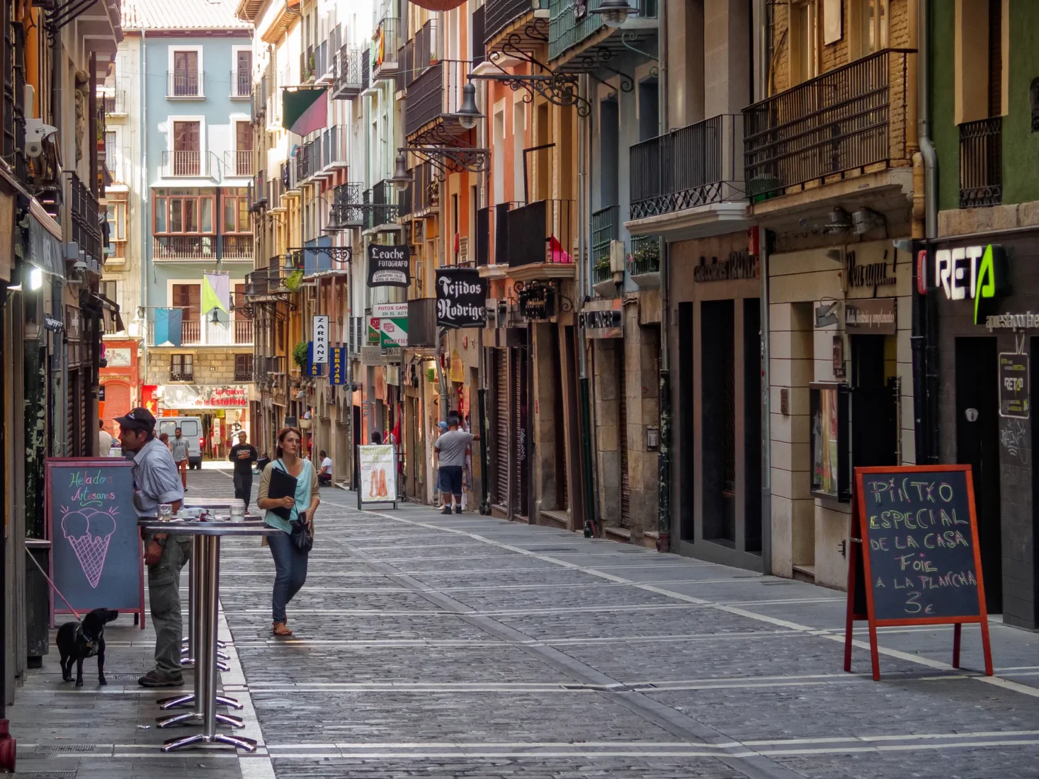 Pamplona'nın tarihi dokusunu yansıtan dar Calle Estafeta sokağında, geleneksel taş binaların gölgesinde yürüyen neşeli kalabalıklar ve canlı sokak kültürü, İspanya'nın enerjik ruhunu ve festival atmosferini hissettiriyor.