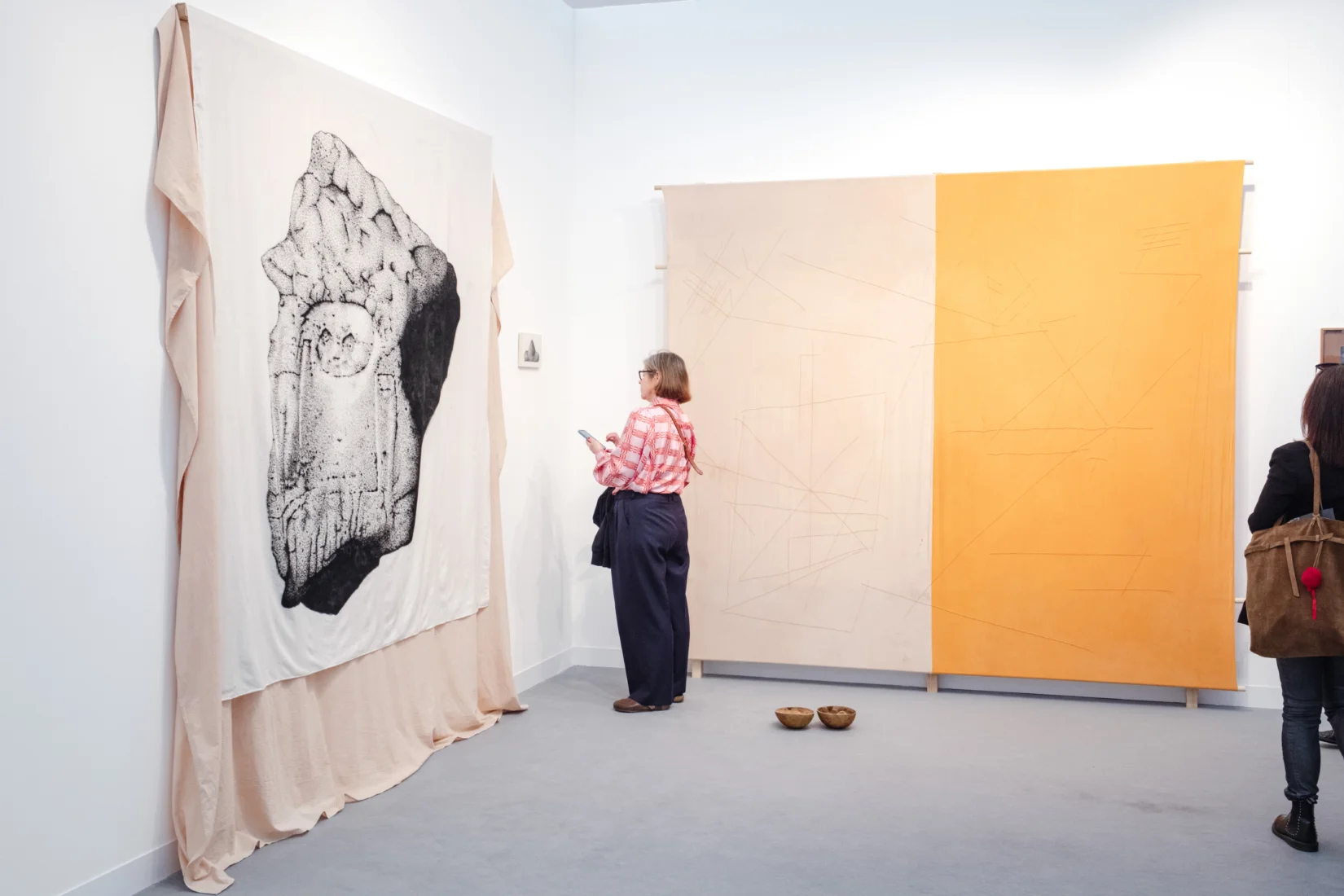 Frieze London'ın Focus bölümünde genç galerileri temsil eden Embajada'nın standında, duvarı kaplayan noktalı siyah beyaz bir kaya kabartması ile yanında pastel pembe ve parlak turuncu renklerde soyut çizgili panellerin önünde duran iki ziyaretçi çağdaş eserleri inceliyor.