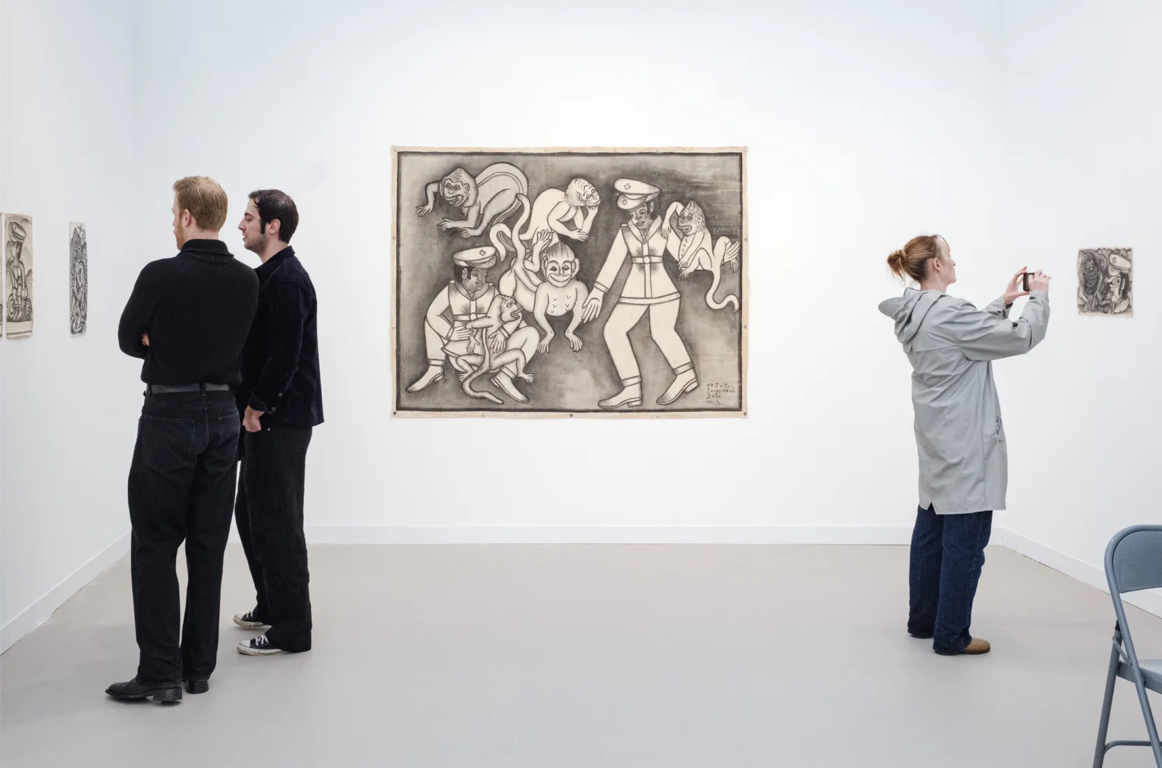 Frieze London'daki The Code Universe bölümünde sergilenen, Endonezyalı sanatçı Oototol'un tuval üzerine Çin mürekkebiyle yaptığı, askerî üniformalı androjen figürlerin yer aldığı eserlerinin beyaz duvarlarda sergilendiği ve 2026 Frieze Stand Ödülü'nü kazanan Valentine galerisinin ışıklı standı, kalabalık bir fuar ortamında izleyicileri ağırlıyor.