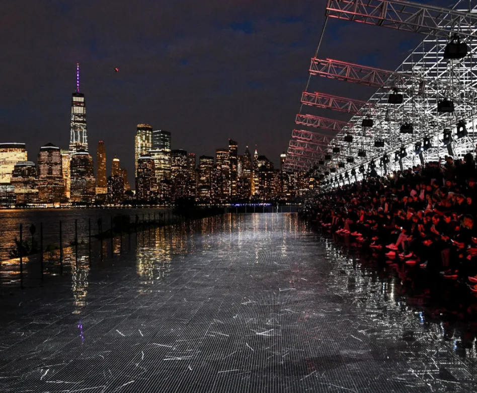 Gece karanlığında Manhattan siluetinin ışıltılarının suya yansıdığı New Jersey kıyısında, Anthony Vaccarello'nun Saint Laurent için düzenlediği unutulmaz defilelerden birinden uzun, metalik bir podyum ve çevresindeki kalabalık görünüyor.