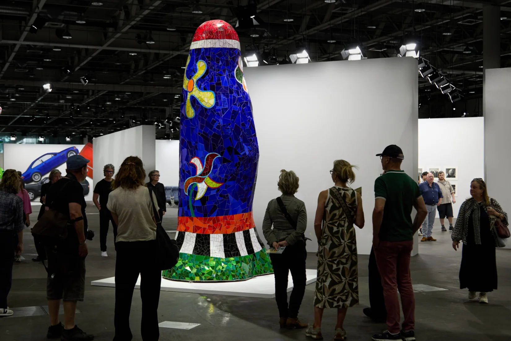 Geniş bir alana yayılmış modern sanat sergisinde, ziyaretçilerin farklı sanatsal ifadeler barındıran eserleri yakından incelediği, sanat piyasasının dinamiklerini gösteren Art Basel ve UBS Küresel Sanat Piyasası Raporu bağlamında bir anı yansıtan canlı ve etkileşimli bir sahne.