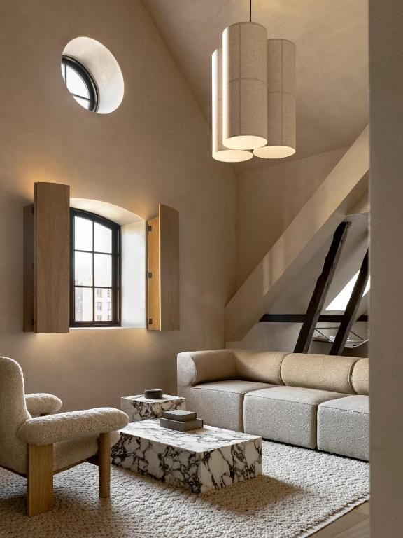 Audo House'un İskandinav minimalist tasarım anlayışını yansıtan bu konforlu yaşam alanında, açık renkli büyük bir kanepe, önünde zarif yuvarlak bir sehpa ve arka planda sade bir şömine, dingin bir atmosfer yaratıyor.