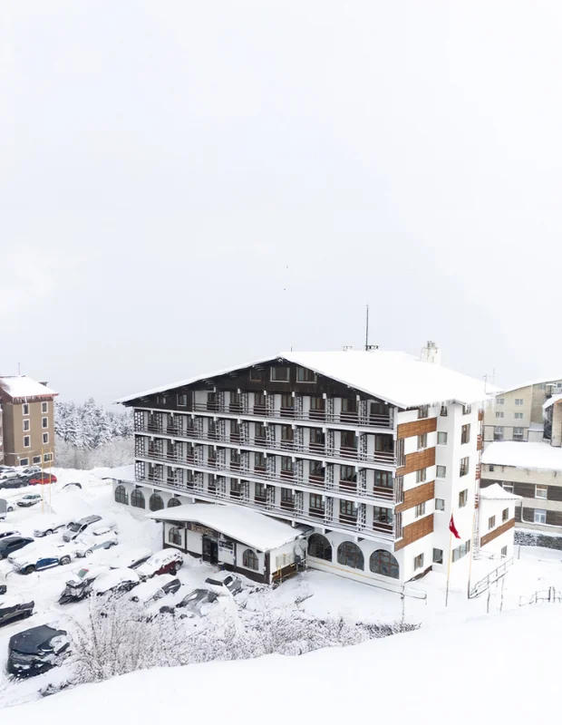Uludağ'ın zirvesinde yer alan ve kış turizminin önemli duraklarından biri olan Beceren Otel'in, çam ağaçları ve bembeyaz karla kaplı dağ manzarası eşliğinde cepheden çekilmiş geniş bir görünümü.