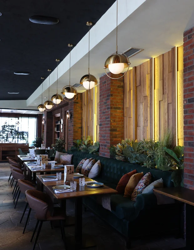 Belgrad'ın ünlü restoranlarından Bela Reka'nın geniş, modern ve zarif iç mekanında, beyaz örtülü yuvarlak masaların ve şık sandalyelerin düzenli bir şekilde yer aldığı aydınlık yemek salonu, tavandan sarkan modern aydınlatmalar ve büyük pencerelerden gelen doğal ışıkla aydınlanıyor.