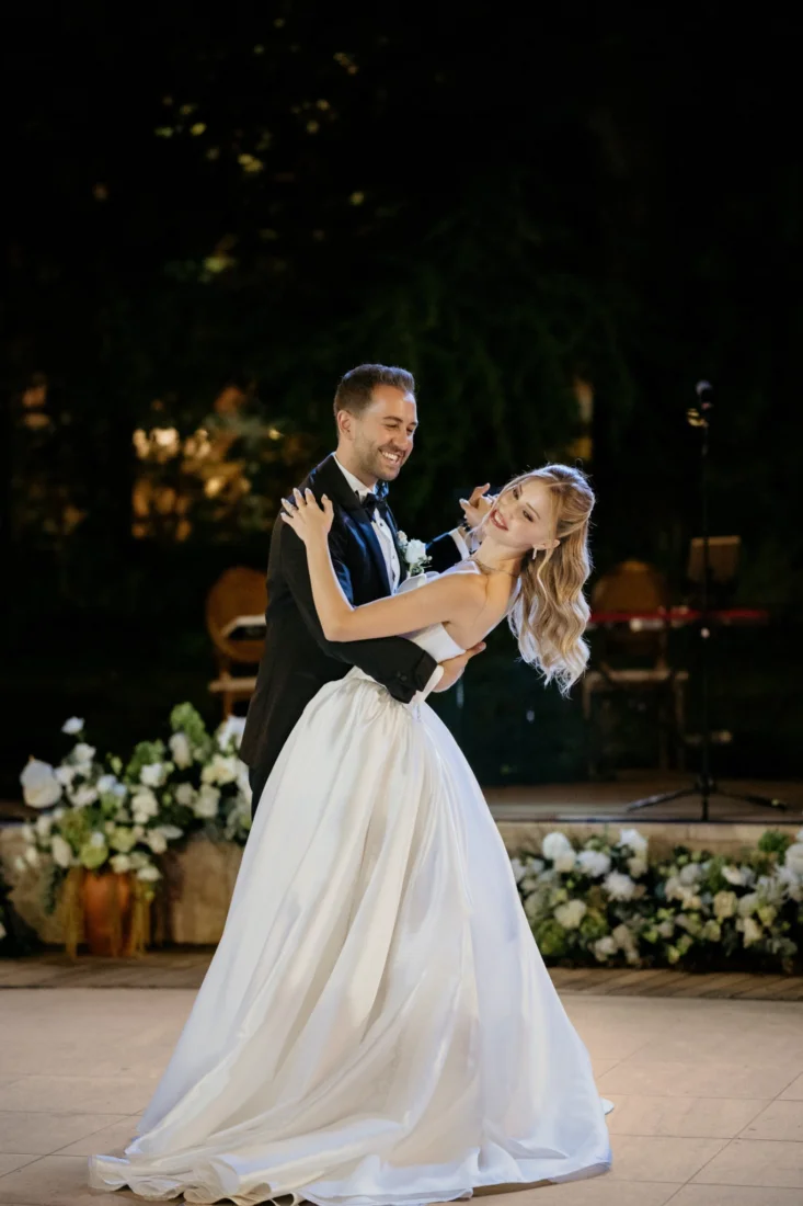 Beril ve Arda'nın düğün hikayesinden bir karede, gelin ve damat olarak şık giysileri içinde, kutlama atmosferinin ortasında, birbirlerine derin bir aşkla ve gözlerinde parlayan sonsuz bir mutlulukla bakarken görülüyorlar.