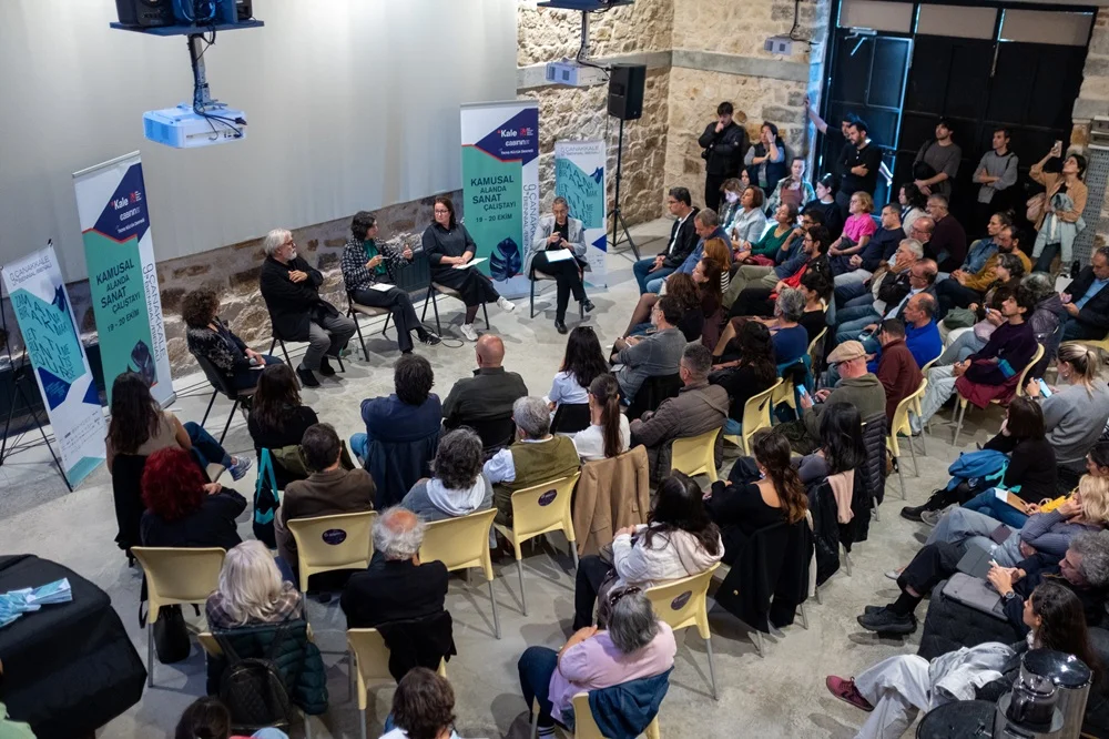 Modern ve geniş bir sanat sergisi salonunda, yumuşak ışıklandırma altında farklı açılardan parlayan metalik ve yansıtıcı yüzeylere sahip, soyut ve büyük ölçekli bir enstalasyon dikkat çekiyor; bu eser, Çanakkale Bienali'nin yenilikçi ruhunu yansıtıyor ve izleyicileri düşünmeye sevk eden bir deneyim sunuyor.
