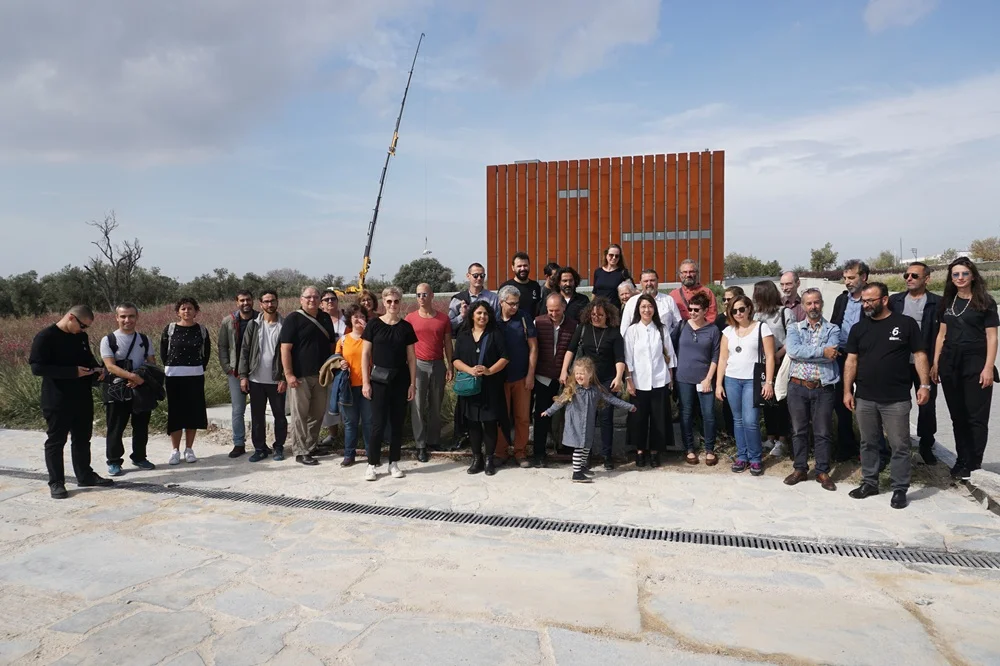 Çanakkale Bienali kapsamında sergilenen, çevredeki gökyüzünün ve doğal manzaranın yansımalarını taşıyan metalik, çok yüzeyli ve keskin hatlara sahip soyut bir dış mekan heykeli, çağdaş sanatın dinamik estetiğini etkileyici bir şekilde sunuyor.