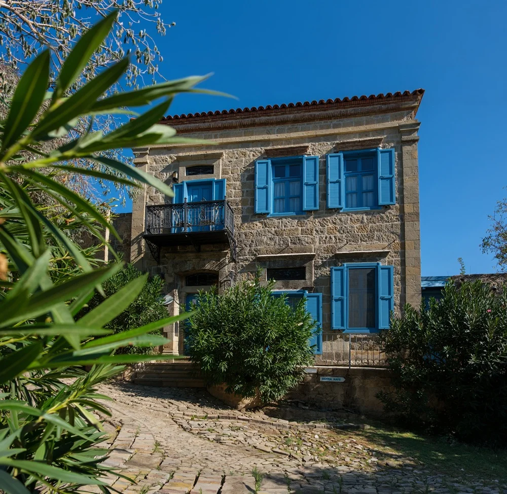Çanakkale Bienali konaklama önerilerinden Adatepe IdaBlue Otel, belirgin mavi dış cephesi, modern çizgileri ve balkonlarıyla yeşillikler içinde, güneşli bir havada ziyaretçilerini bekleyen estetik bir yapıyı gözler önüne seriyor.