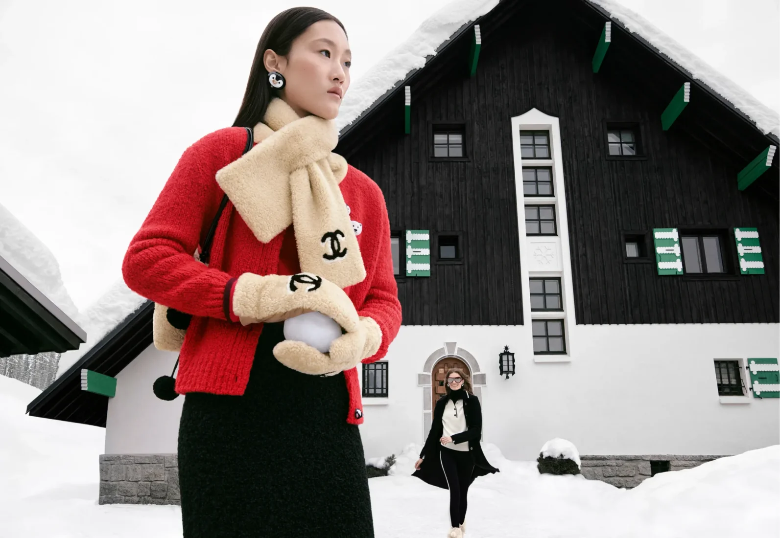 Karlı bir dağ evinin önünde, kırmızı hırkası, üzerindeki Chanel logosuyla bej renkli polar atkısı ve eldivenleriyle bembeyaz bir kar topu tutan model, Chanel Coco Neige koleksiyonunun retro kayak modasına getirdiği rahat ve şık kış stilini yansıtıyor.