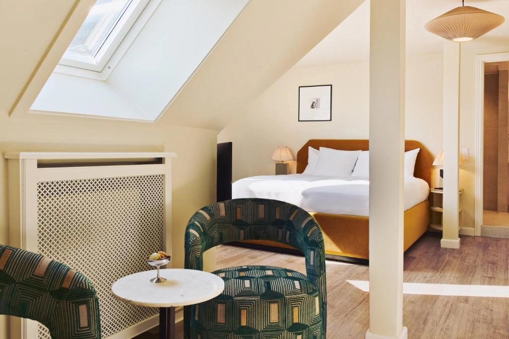 Coco Hotel'in zarif ve modern bir şekilde dekore edilmiş geniş odasında, bembeyaz çarşaflarla kaplı konforlu bir yatak, ahşap detaylarla zenginleşen şık mobilyalar ve huzurlu bir atmosfer sunan büyük pencereden görünen davetkar manzara, misafirler için unutulmaz bir konaklama deneyimi vadediyor.