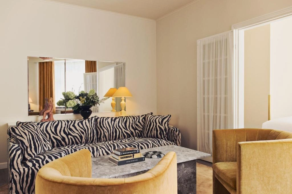 Coco Hotel'in çağdaş tasarım anlayışını yansıtan, aydınlık ve ferah bir otel odasında, sade ve şık detaylarla dekore edilmiş geniş yatak, modern komodin ve atmosferik aydınlatmalarla zenginleştirilmiş, konuklarına huzurlu bir lüks konaklama deneyimi sunan zarif bir ambiyans göze çarpıyor.