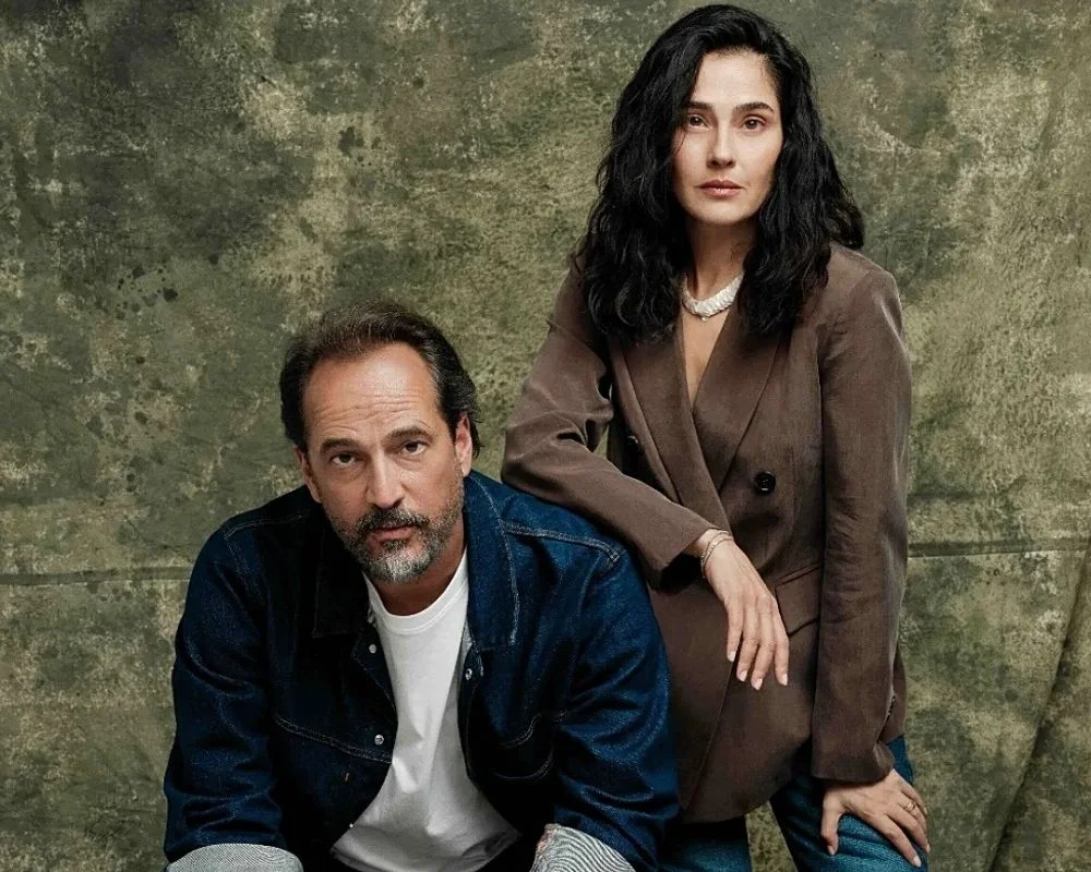 Minimalist bir tiyatro sahnesinde dramatik ışıklandırma altında, oyuncular Timuçin Esen ve Funda Eryiğit, Maja Zade'nin Değişim / Dönüşüm oyununda evlilikteki zorlu yüzleşmeleri ve canlandırdıkları 22 farklı karakteri sergiliyor.