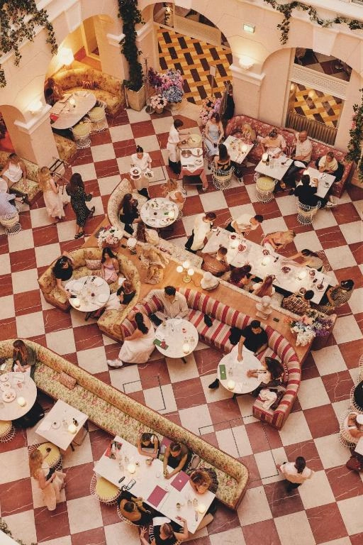Hotel Bella Grande'nin şık restoranında, beyaz masa örtüleriyle kaplı, zarif porselen tabaklar, gümüş çatal bıçak takımları, parlak kadehler, yanan mumlar ve taze çiçek aranjmanlarıyla özenle hazırlanmış, davetkar bir akşam yemeği masası düzenlemesi, arka planda hafif perdelerle süslenmiş pencerelerin doğal ışığıyla parlıyor.