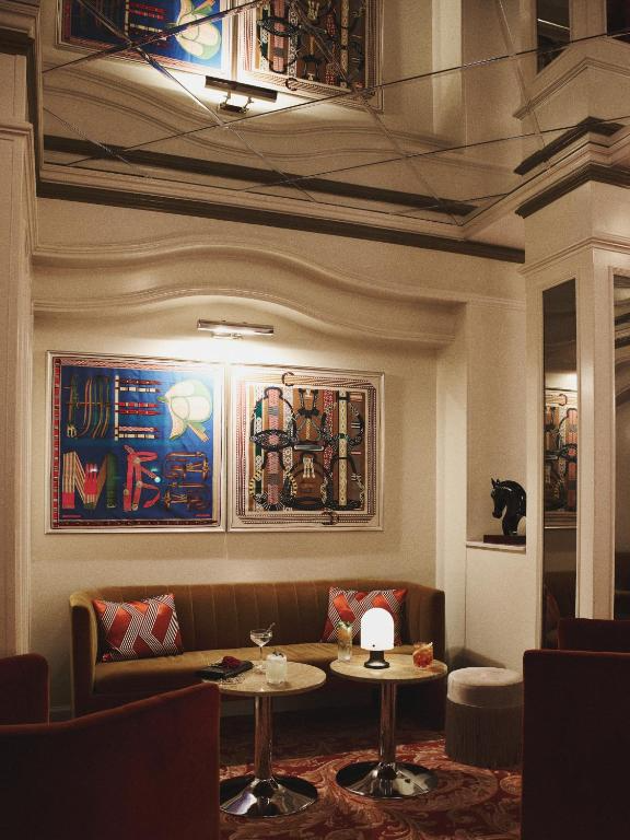 Hotel Bella Grande'nin panoramik şehir manzarasına sahip, modern ve zarif bir şekilde döşenmiş lüks suitinde, takım elbiseli bir beyefendinin pencereden dışarıyı seyrettiği, huzurlu ve geniş bir yaşam alanı tasviri.