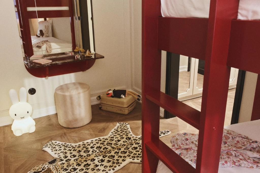 Hotel Bella Grande'nin zengin dekore edilmiş salonunda, ortada iki konforlu koyu renk koltuk arasında yükselen gösterişli, detaylı işlemeli taş şömine ve üzerinde yer alan büyük, varaklı ayna, mekanın lüks ve davetkar atmosferini kusursuzca yansıtır.