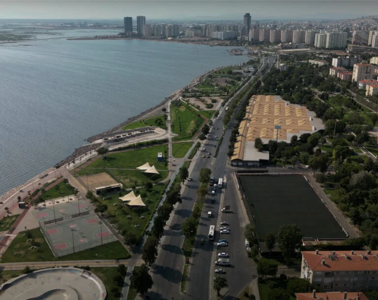Karşıyaka Kent Müzesi'nin açık hava sergileme bölümünde, güneşin aydınlattığı geniş bir alanda, antik dönemlere ait olduğu anlaşılan büyük taş eserlerin ve heykellerin titizlikle yerleştirildiği, yeşil bitki örtüsüyle çevrili, ziyaretçilere dingin bir kültürel deneyim sunan detaylı bir görünüm.