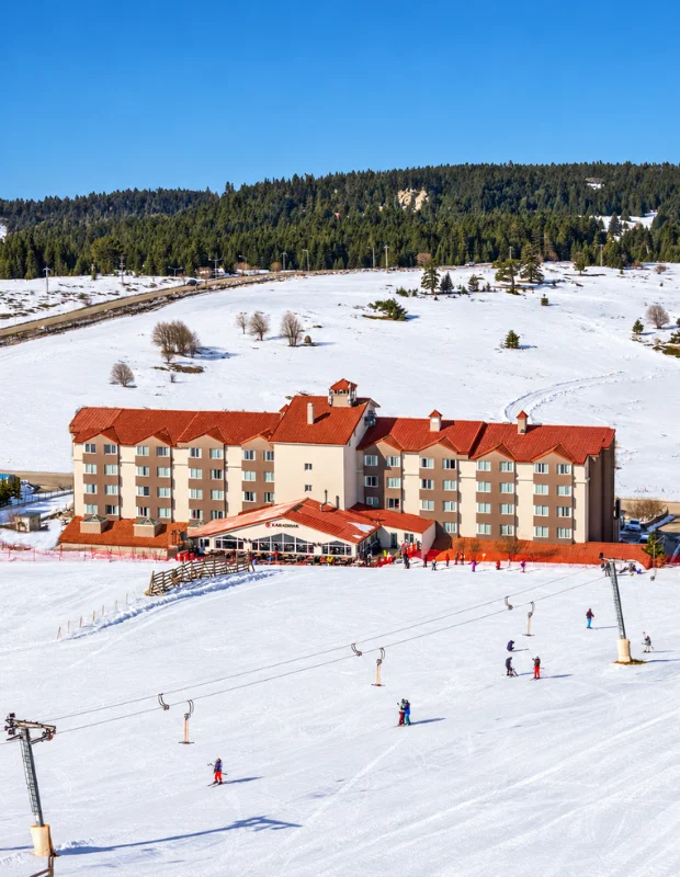 Kaya Otel'in çağdaş ve şık mimarisiyle tasarlanmış, doğal ışıkla aydınlanmış geniş lobisinde, uzun resepsiyon masasının arkasında misafirleri bekleyen personel ve konforlu oturma alanları, otelin lüks ve davetkar atmosferini yansıtıyor.