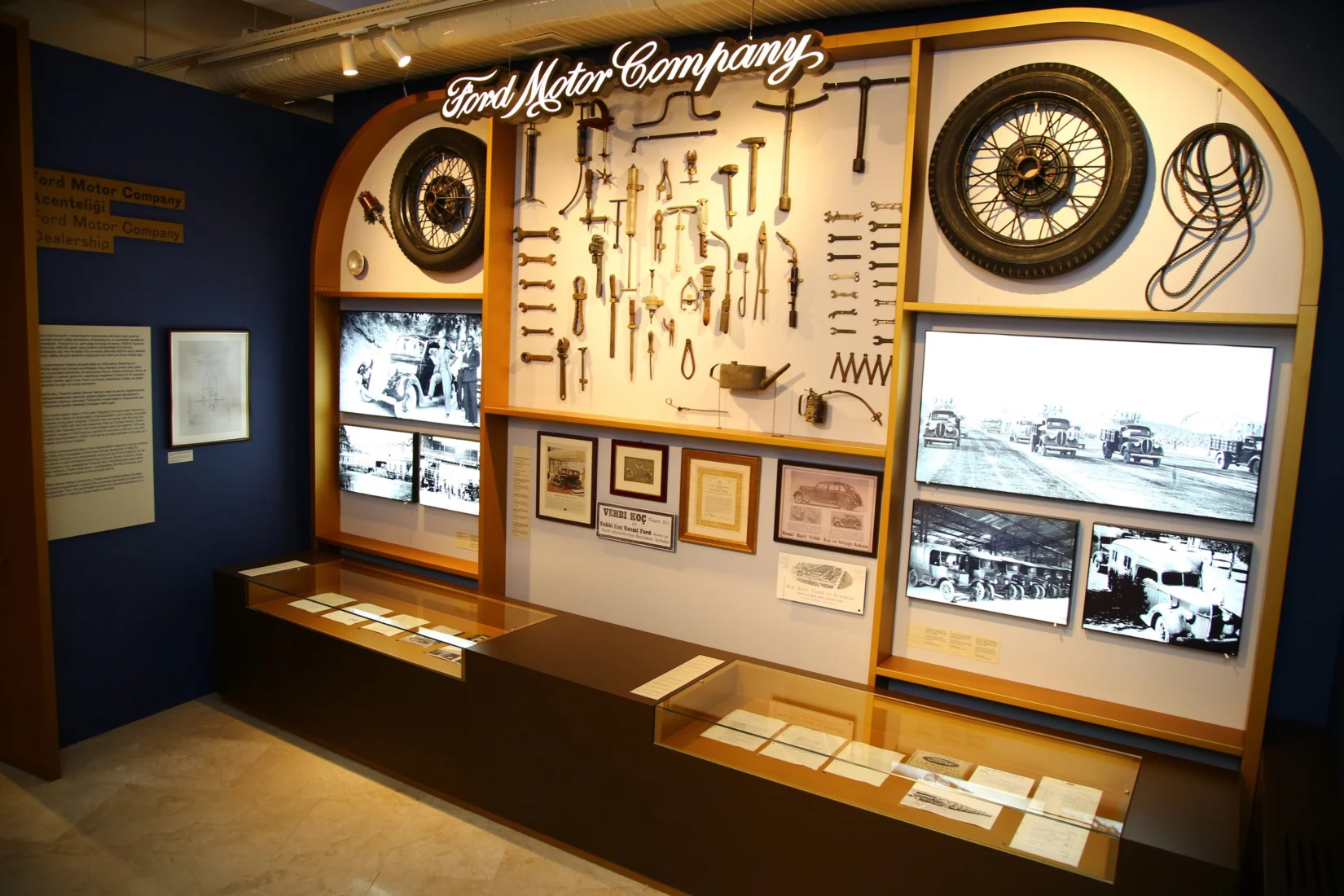 Parlak ışıklı bir sergi salonunda, Koç Sergisi kapsamında özenle konumlandırılmış ve Koç ile Ford Motor arasındaki derin iş birliğini yansıtan, farklı dönemlere ait klasik Ford otomobillerini ilgiyle inceleyen ziyaretçiler gözüküyor.