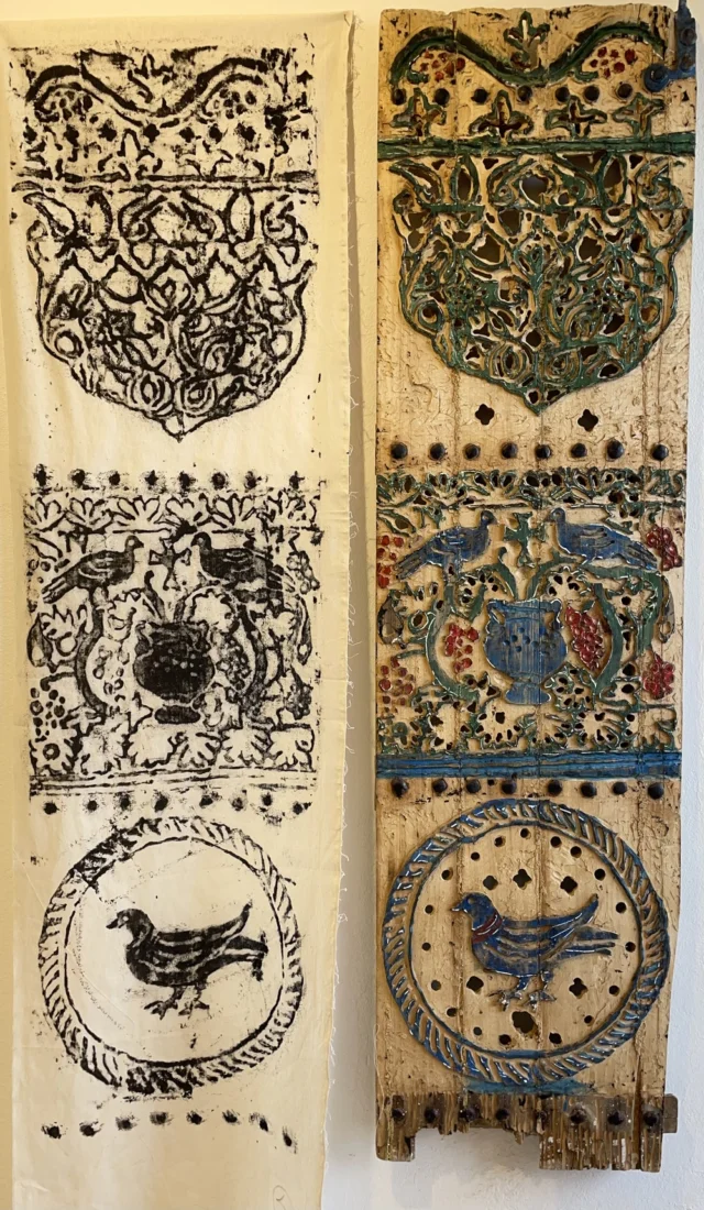Elnaz Rahimoğlu, Lenzart Space'teki röportajı sırasında modern ve şık bir ortamda, yüksek bir sandalyede oturmuş, koyu renkli, desenli bir üst giysi ve üzerine blazer ceketle kameraya gülümseyerek poz veriyor.