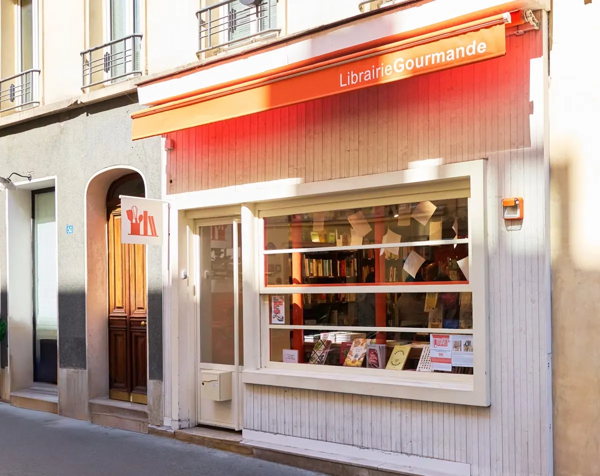 Paris'teki Rue Vavin'de yer alan ve turuncu tenteli Librairie Gourmande adlı özel bir gastronomi kitapçısının dış cephesi, geniş vitrininde sergilenen binlerce yemek kitabı ve nadir gastronomi yayınıyla dikkat çekiyor.